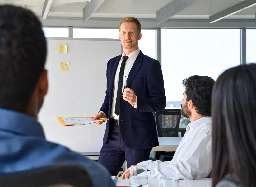 Business man presenter team leader wearing suit giving presentation training on whiteboard in office. Male company executive manager presenting corporate strategy at group conference meeting.