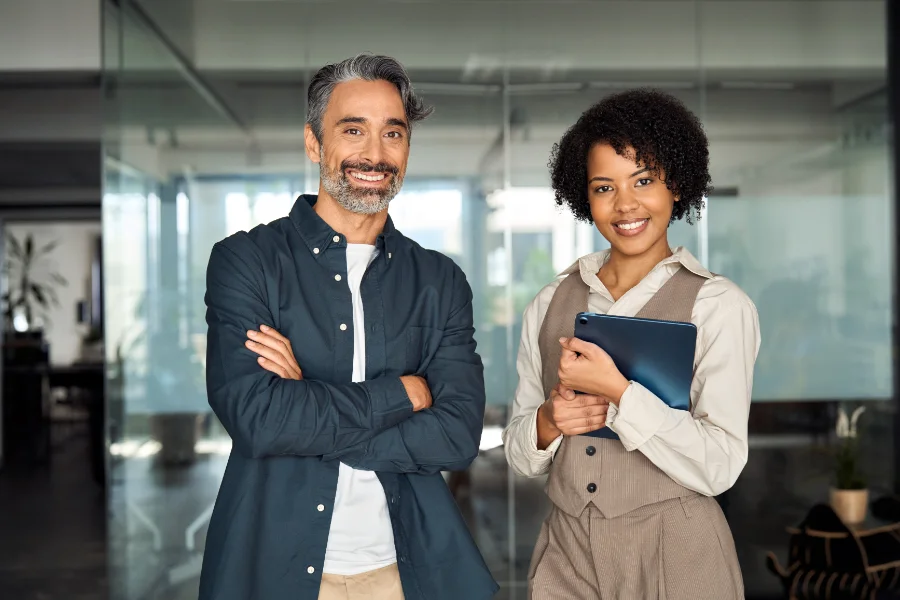 Two diverse business partners, employees or executives standing in office looking at camera. Man and woman sales managers, company workers, consultancy professionals posing for corporate portrait.