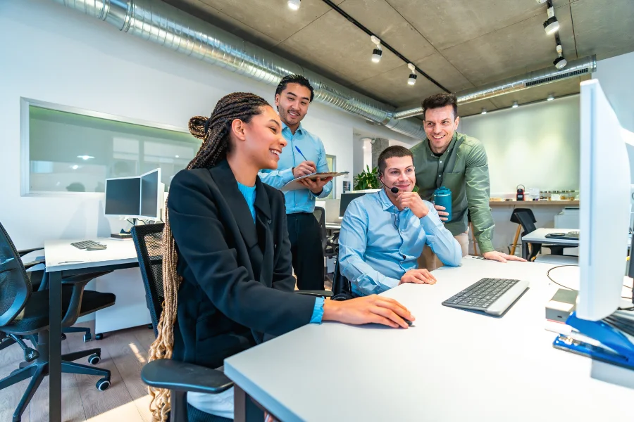 Diverse colleagues gather around a computer, engaging in teamwork and problem solving within a contemporary office setting